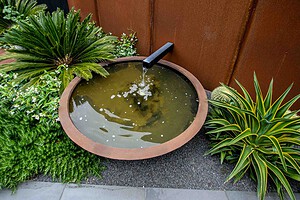 Circular copper-rimmed water feature with black spout surrounded by tropical plantings in Brighton East courtyard