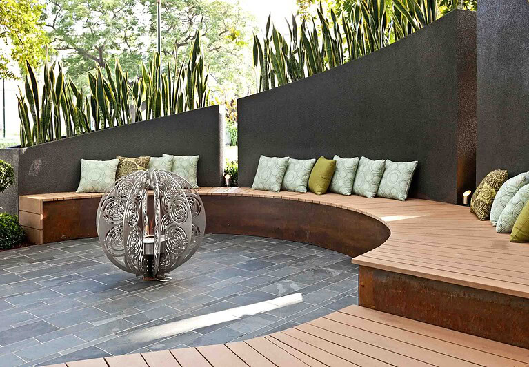 Curved timber bench seating with green cushions around decorative water feature in contemporary Melbourne show garden