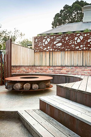 Circular swimming pool with central corten steel fire pit surrounded by curved timber decking and tiered seating areas