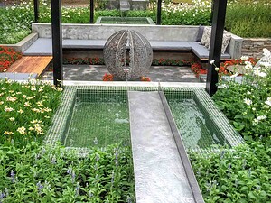 Geometric water feature with circular leaf sculpture and mosaic tiles, surrounded by flowering plants in Nagasaki garden