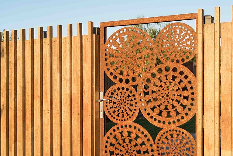 Custom corten steel garden gate with circular perforated pattern in timber fence frame at Buninyong residence