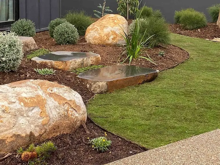 Basalt stone steppers floating through mulched garden beds with large sculptural boulders at Daylesford Block house