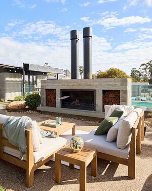 Modern concrete fireplace with timber outdoor furniture and pool backdrop at Daylesford House 5 from The Block