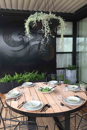 Round blackbutt timber dining table with black steel chairs on rooftop terrace overlooking St Kilda