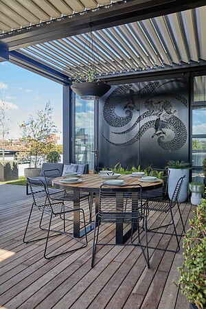 Modern rooftop dining area with blackbutt decking, round timber table, wire chairs and dragon wall art in St Kilda