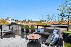 Grey sectional sofa with blue cushions on rooftop terrace overlooking St Kilda cityscape with round timber coffee table