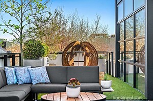 Grey sectional sofa with blue cushions on rooftop terrace with circular art piece and city views in St Kilda