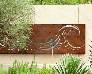 Corten steel wall panel with wave cut design mounted against rendered garden wall with planting