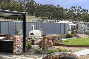 Curved exposed aggregate paths connecting outdoor entertaining area with pizza oven and native plantings in Gisborne