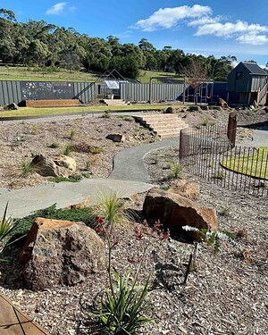 Curved exposed aggregate pathways wind through native plantings with large basalt boulders in Gisborne country garden