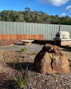 Outdoor brick pizza oven with timber seating and exposed aggregate paving in Gisborne Macedon Ranges garden