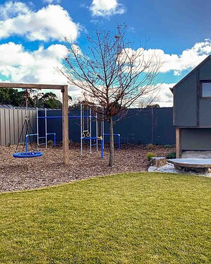 Blue playground equipment on mulched surface with exposed aggregate paths curving through Gisborne country garden