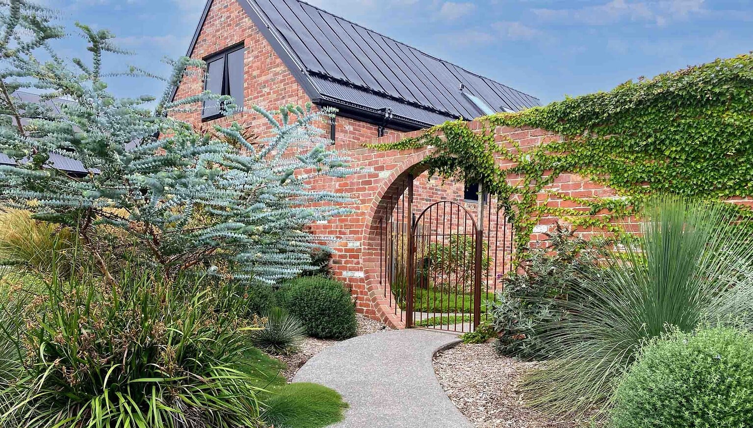 Curved brick archway entrance with steel gate leading through native plantings at Mount Buninyong country garden