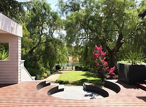 Curved timber deck with built-in circular firepit seating area overlooking landscaped garden with mature trees