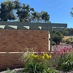 Modern brick pavilion with steel pergola frame surrounded by colorful native plantings and gravel pathways